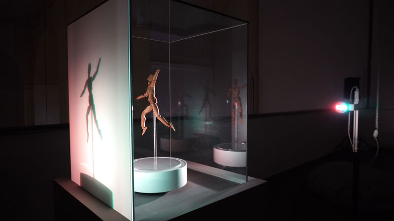 An original mannequin from Christian Schad's archive rotates in front of a red and blue light source, casting a double shadow.